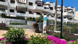 A multi-story building with balconies, a paved area with benches, and a signpost. - Modern apartment in San Juan de los Terreros with pool and air conditioning (San Juan de los Terreros)