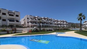 A swimming pool with a lifebuoy, surrounded by a landscaped area with palm trees and a building complex in the background. - Modern apartment in San Juan de los Terreros with pool and air conditioning (San Juan de los Terreros)