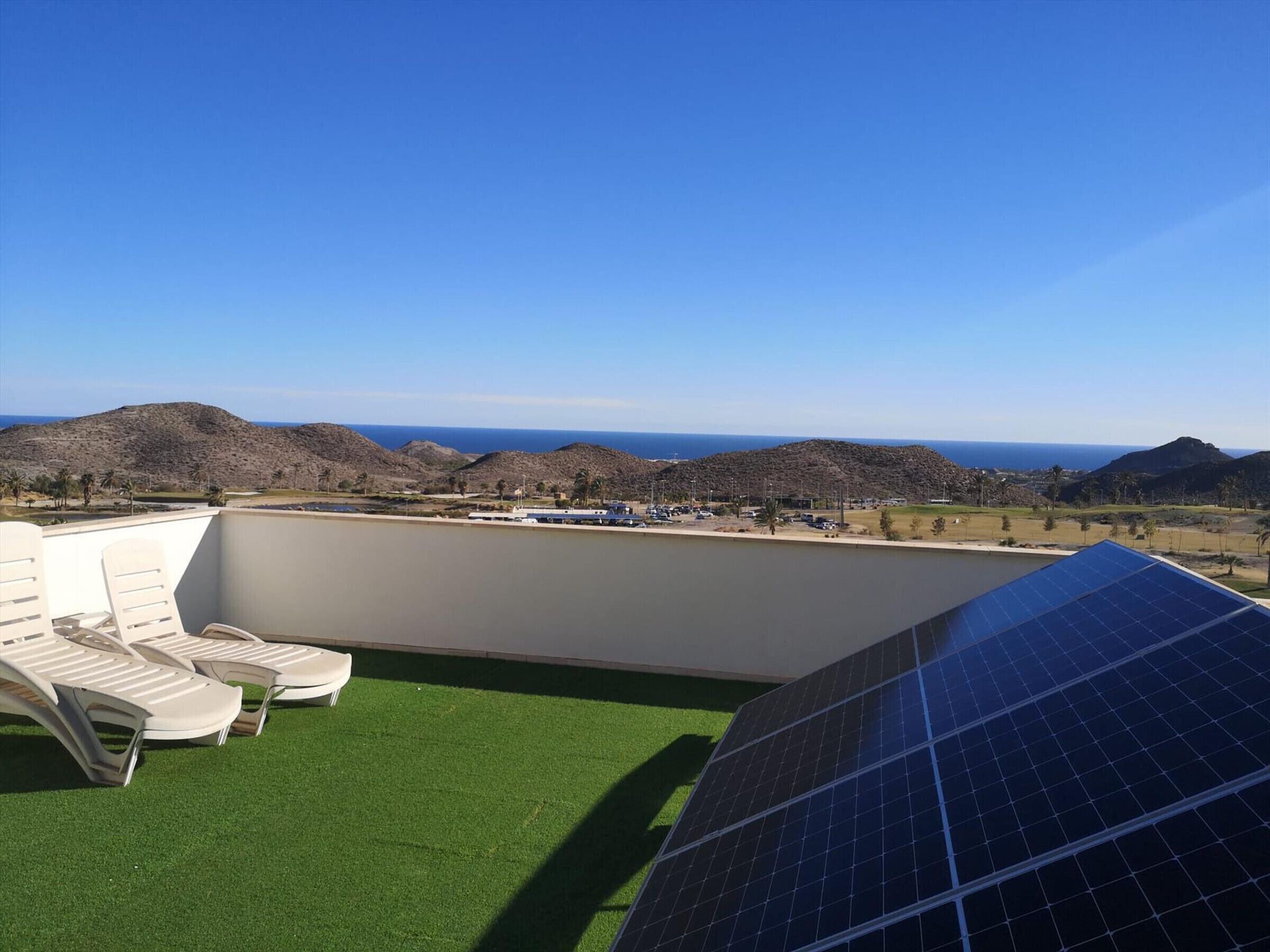 Terraza en la azotea con vista al mar, paneles solares y sillones de descanso.