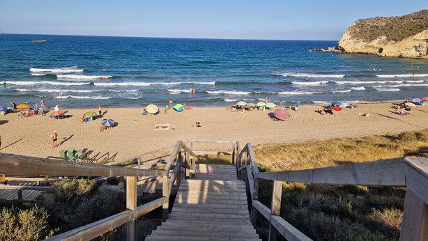 A wooden staircase leading to a sandy beach with umbrellas and people. - Comfortable Apartment in Pulpí, Andalusia, 2 Bedrooms (Pulpí)