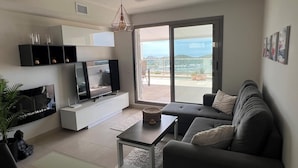 A modern living room with a flat-screen TV, a sofa, a coffee table, and a view of the outdoors through a sliding glass door. - Comfortable Apartment in Pulpí, Andalusia, 2 Bedrooms (Pulpí)