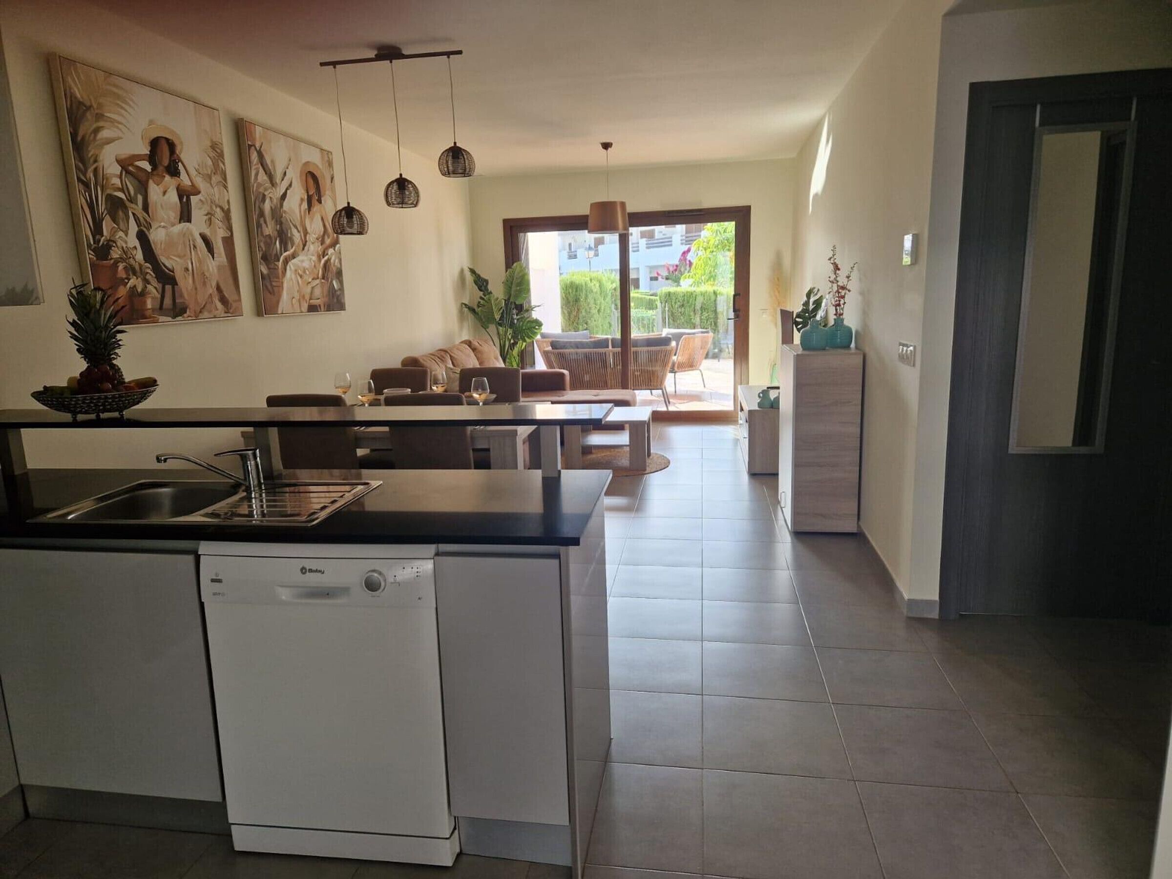 A modern kitchen with a dishwasher, dining area with a sofa and chairs, and a living room with a couch and a coffee table.