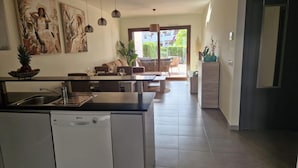 Una cocina moderna con lavavajillas, comedor con sofá y sillas, y sala de estar con sofá y mesa de centro.