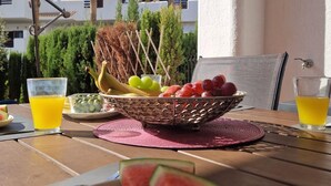 Una mesa servida con una cesta de frutas, vasos de jugo de naranja y una rebanada de sandía.