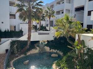 Une piscine entourée de palmiers et un bâtiment blanc doté de balcons.