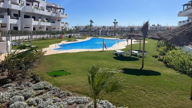 A swimming pool surrounded by a well-maintained lawn, with modern buildings in the background. - Charming apartment in San Juan de los Terreros (San Juan de los Terreros)
