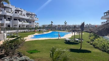 Una piscina rodeada de un césped cuidado, con edificios modernos al fondo.