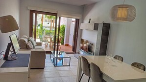 A modern living room with a sofa, coffee table, TV, and dining area with chairs and wine glasses. - Charming apartment in San Juan de los Terreros (San Juan de los Terreros)