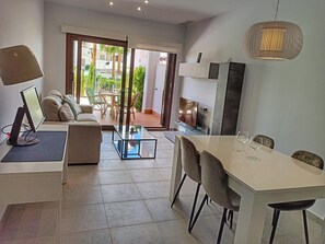 Un salon moderne comprenant un canapé, une table basse, un téléviseur et un coin repas avec des chaises et des verres à vin.