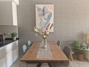 Un comedor con una mesa de madera, sillas, un jarrón con flores y una obra de arte de plumas de gran tamaño en la pared.