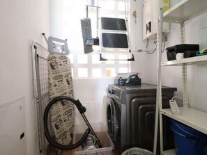 Un lavadero con lavadora, secadora, aspiradora y un estante con productos de limpieza.