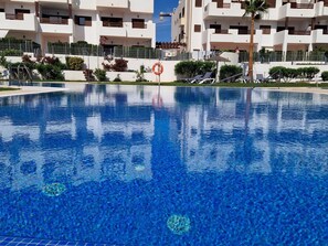 A clear blue swimming pool with lounge chairs and a lifebuoy sign, surrounded by white buildings with balconies and palm trees. - Modern apartment in San Juan de los Terreros, near beach and pool (San Juan de los Terreros)