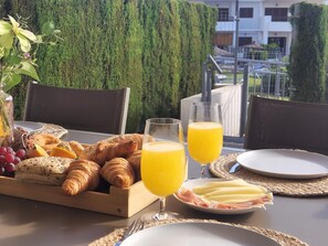 A breakfast setting with croissants, cheese, grapes, and orange juice on a terrace with a view of a building and greenery. - Modern apartment in San Juan de los Terreros, near beach and pool (San Juan de los Terreros)