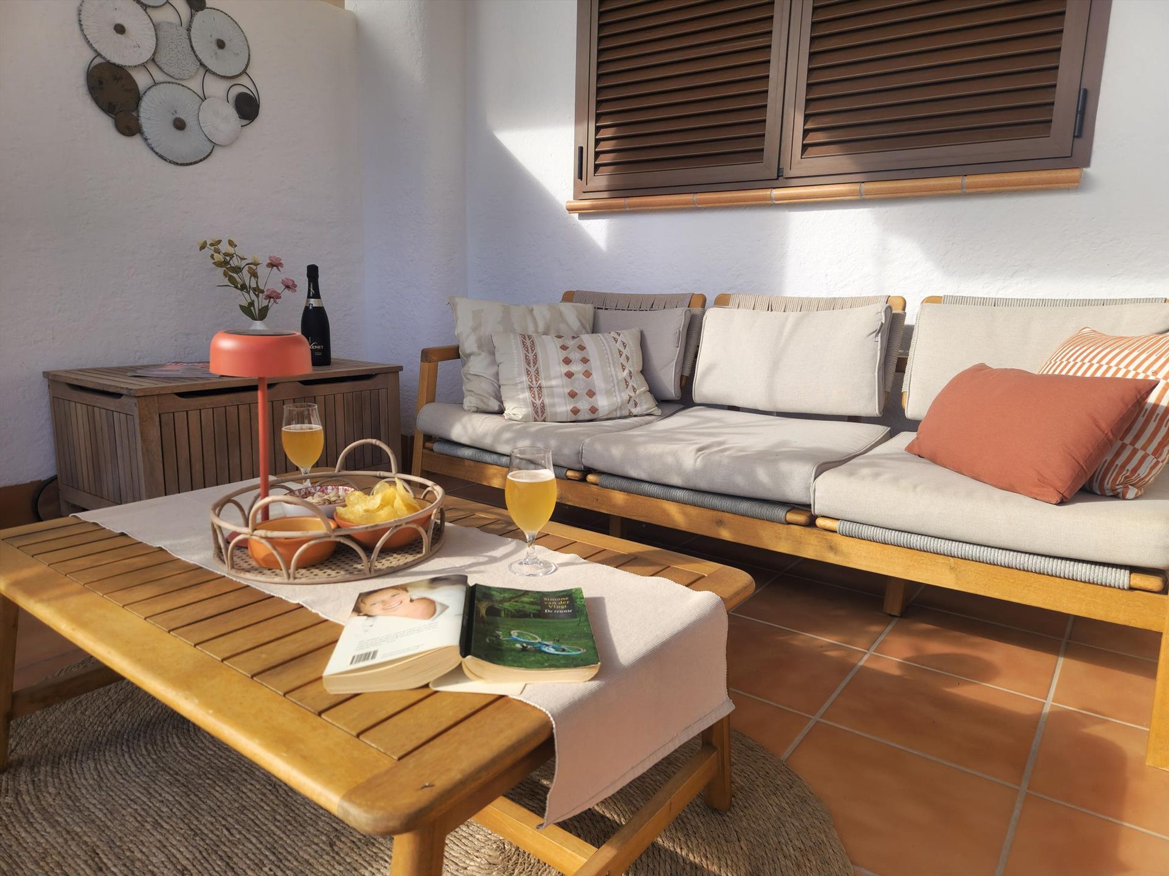 Un salon chaleureux avec un canapé en bois, une table basse sur laquelle reposent un livre et des lunettes, et un élément décoratif mural.