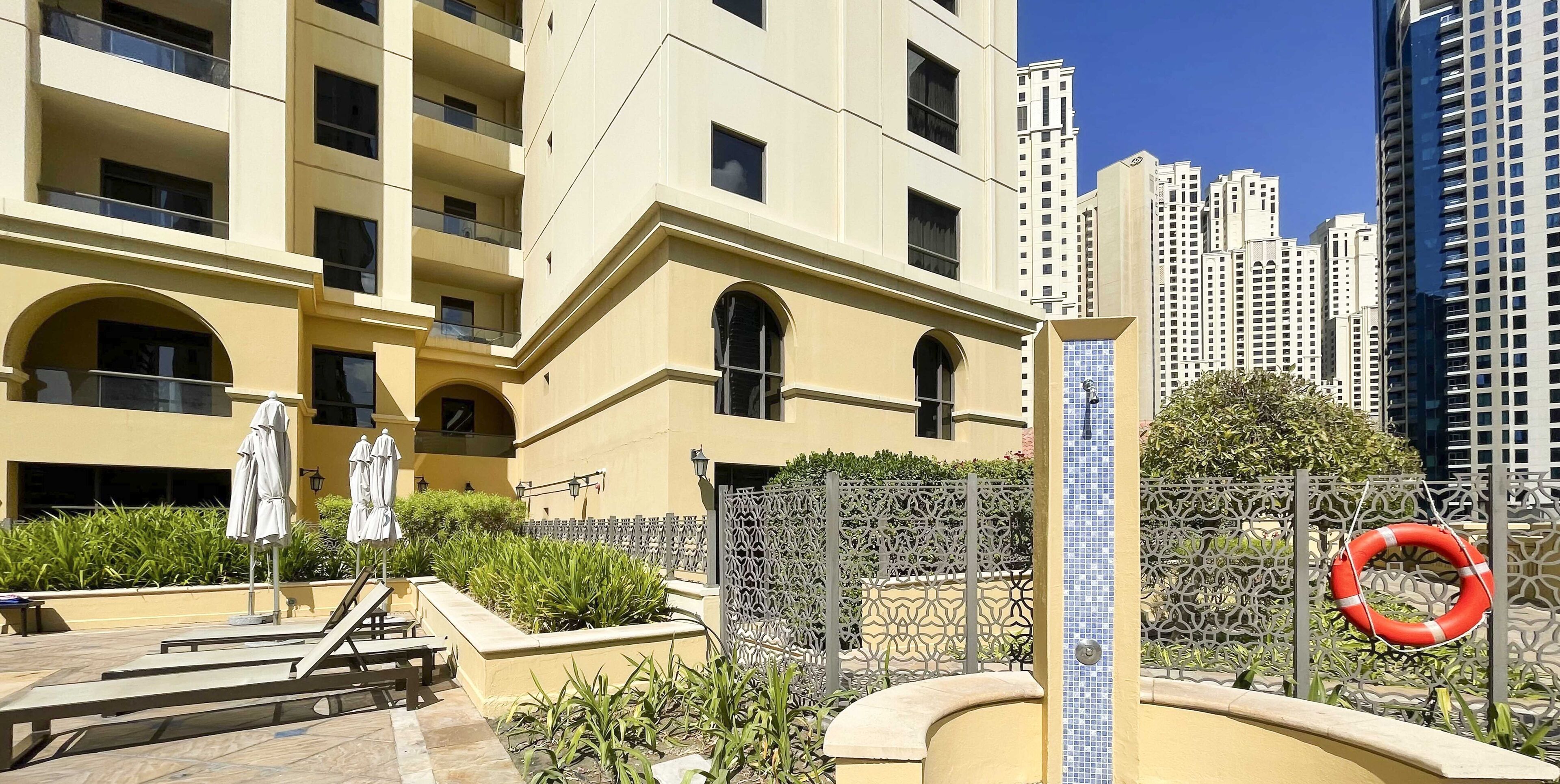 A modern building with multiple balconies, outdoor seating, and a decorative fence.