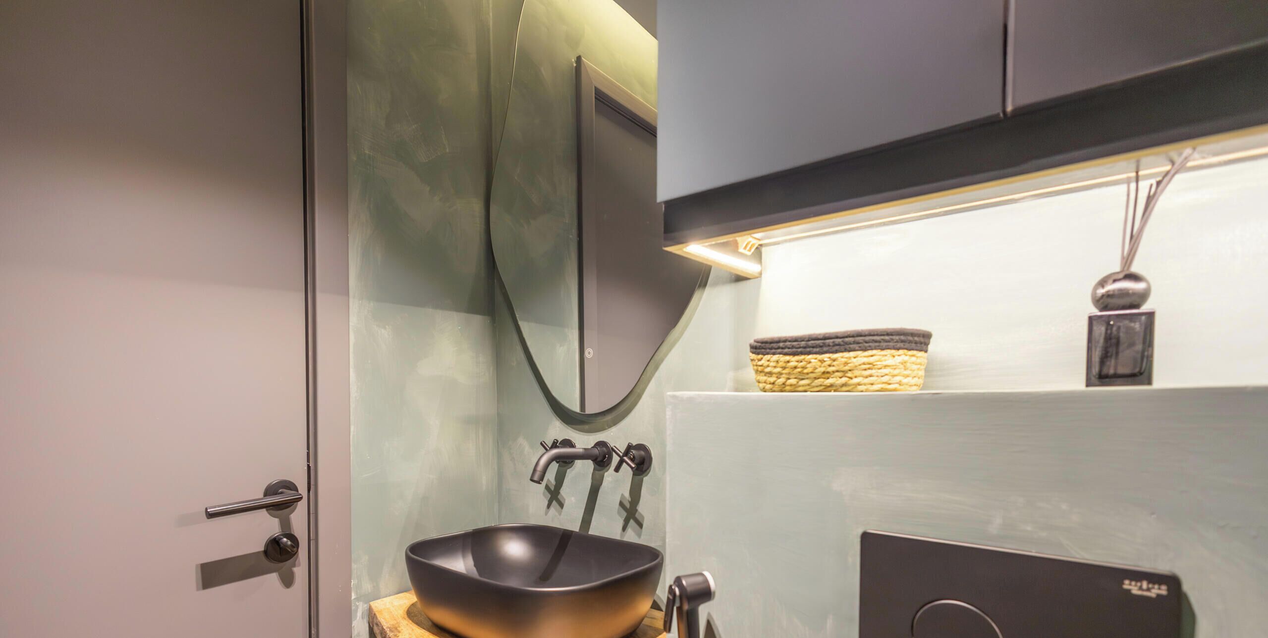 A modern bathroom with a black vessel sink, a towel rack, and a basket on the wall.