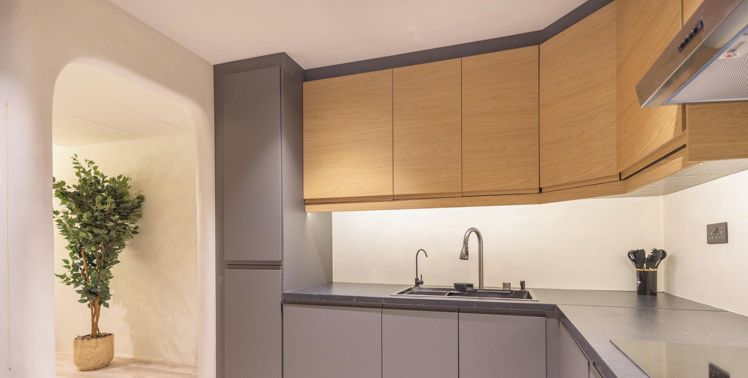 A modern kitchen with grey cabinets, a wooden countertop, a built-in sink, and a potted plant.