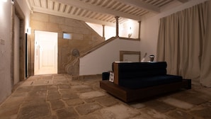 A stone-floored room with a staircase, a dark blue sofa, and a wooden cabinet. - Ando Living - São Miguel House - 203 (Porto)