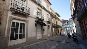 A narrow cobblestone street lined with historic buildings, featuring a prominent building with a large window and a sign that reads "ANDO Living." - Ando Living - São Miguel House - 203 (Porto)