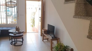 Ett vardagsrum med en soffa, ett runt bord, en tv på ett tv-bord och korgar av rotting.