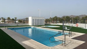 En swimmingpool med ett livräddartorn, omgiven av ett inhägnat område med fri sikt mot bergen i bakgrunden.