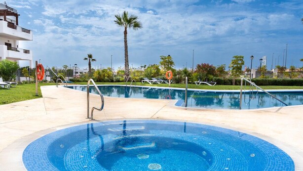 Una piscina con jacuzzi, rodeada de sillones de descanso y palmeras.