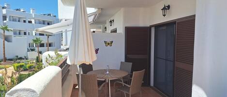 A balcony with a table and chairs, a white umbrella, and a view of buildings in the background.