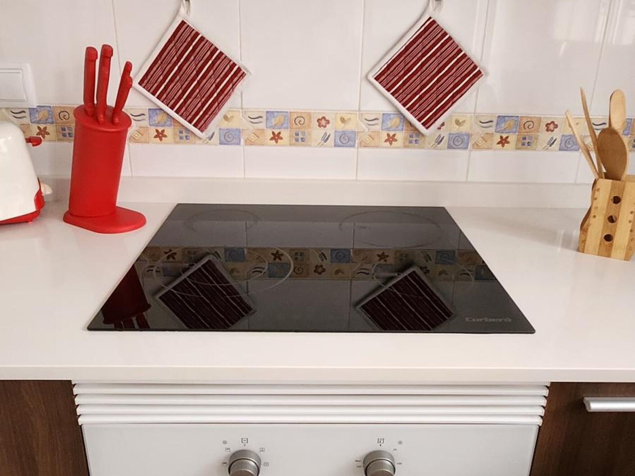 A kitchen with a black induction cooktop, white cabinets, and a patterned backsplash.