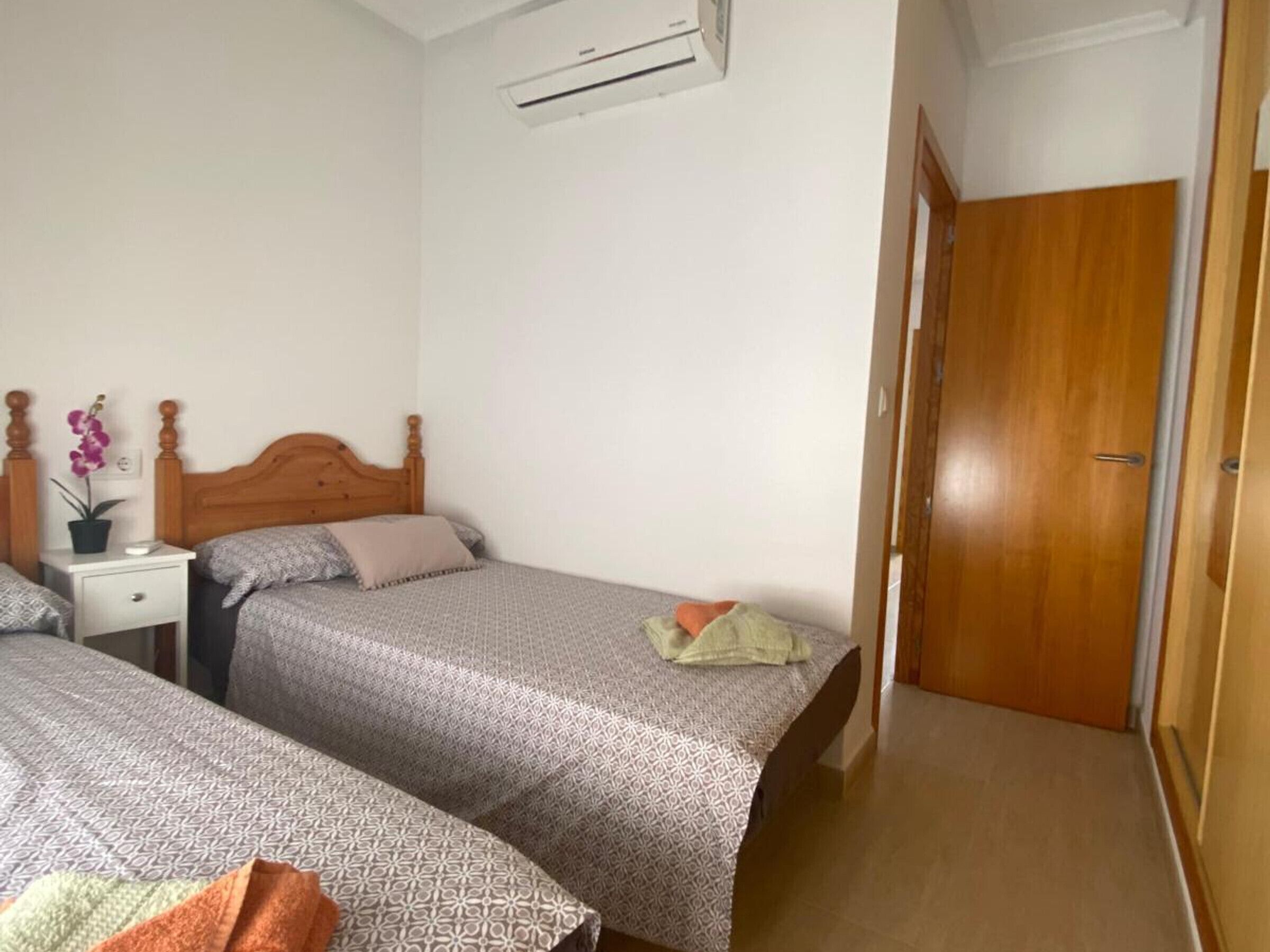 Un dormitorio con dos camas, una mesita de noche, una orquídea en maceta y una puerta de madera.