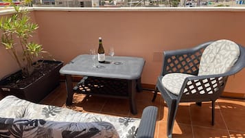 Ein Balkon mit Tisch, zwei Stühlen, einem Blumentopf und einer Weinflasche.