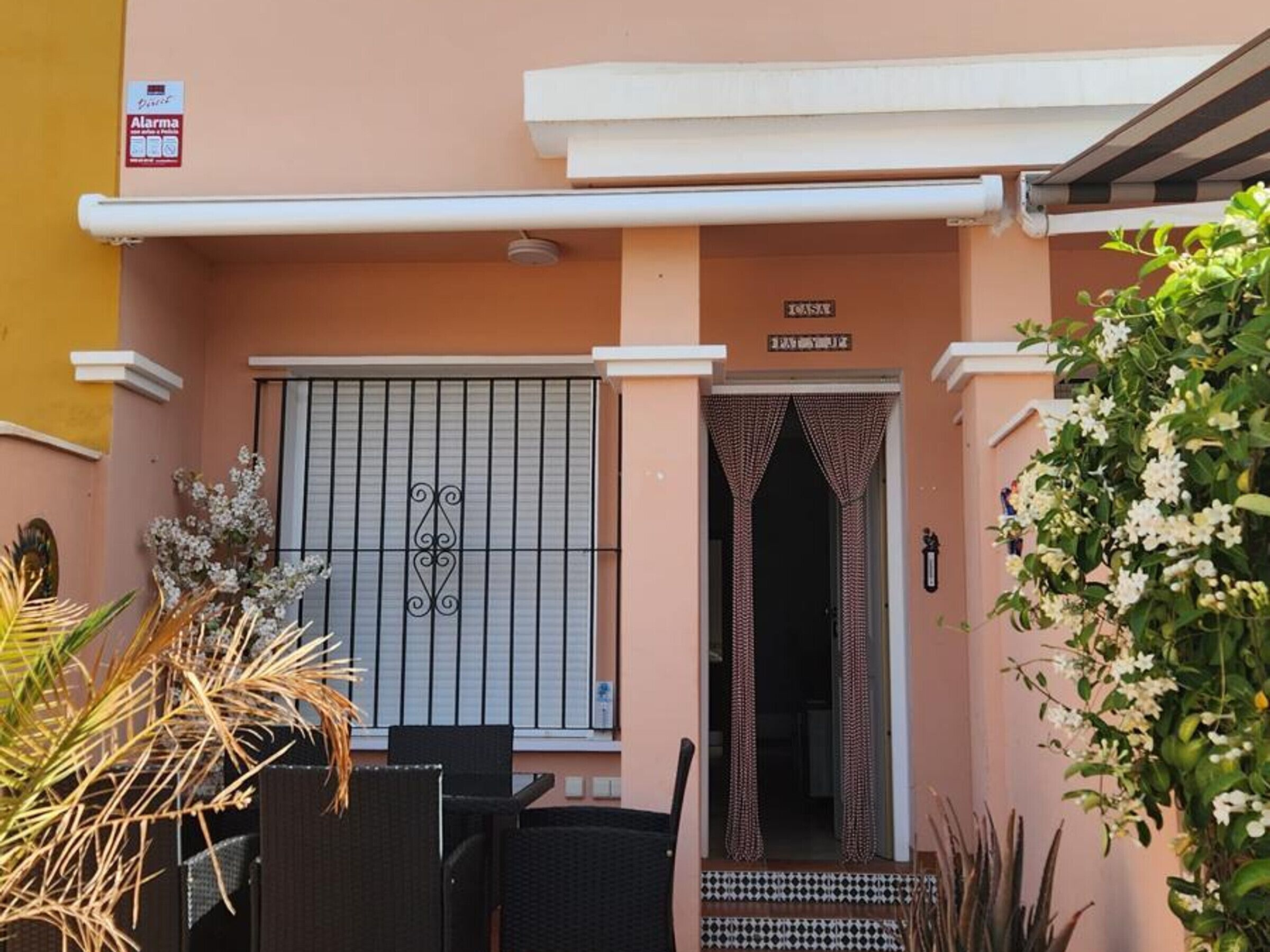 A building entrance with a metal gate, a small porch with chairs, and a sign above the door.