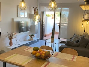 A modern living space with a dining area, a sofa, a TV, and a balcony with a view. - Charming apartment 200m from beach with communal garden (San Juan de los Terreros)