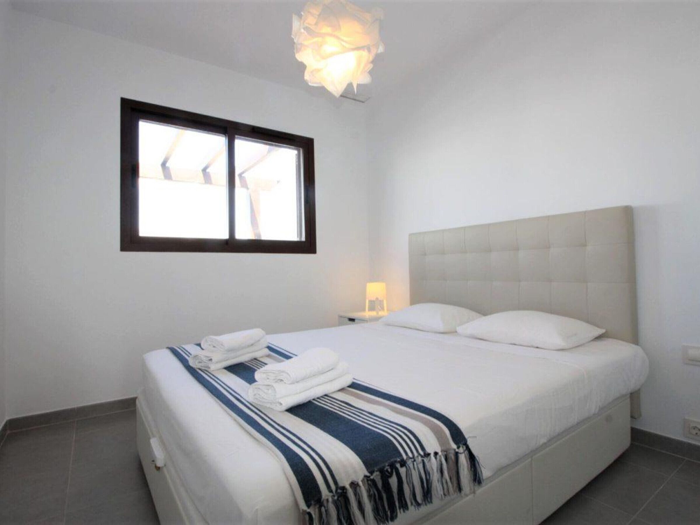 Een slaapkamer met een bed, een raam en een nachtkastje met een lamp.