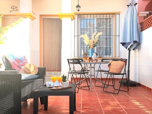 Um pátio ensolarado com uma mesa de jantar, cadeiras e um sofá de vime.