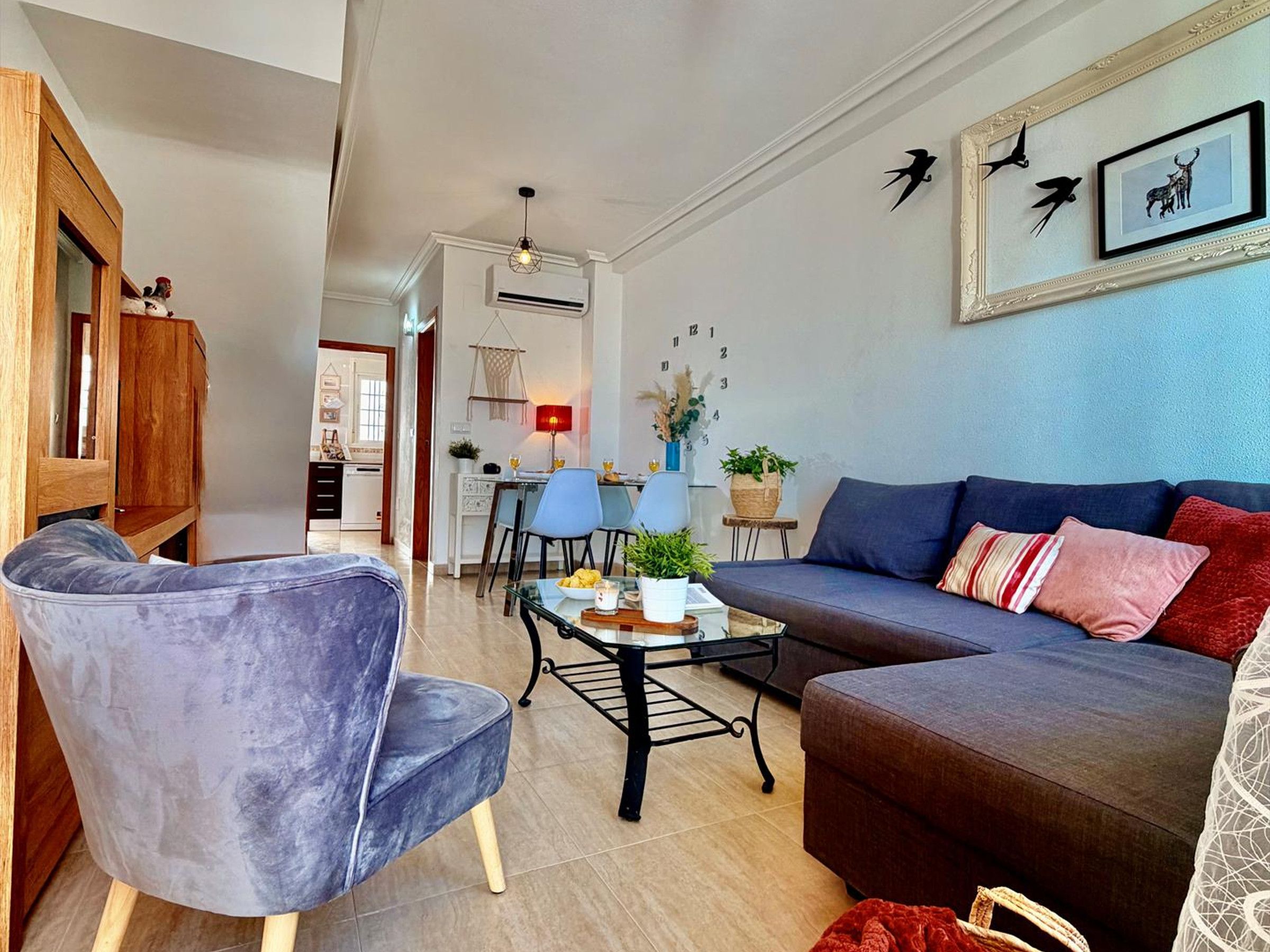 A living room with a sofa, armchair, and coffee table. There is a dining area in the background with a table and chairs.
