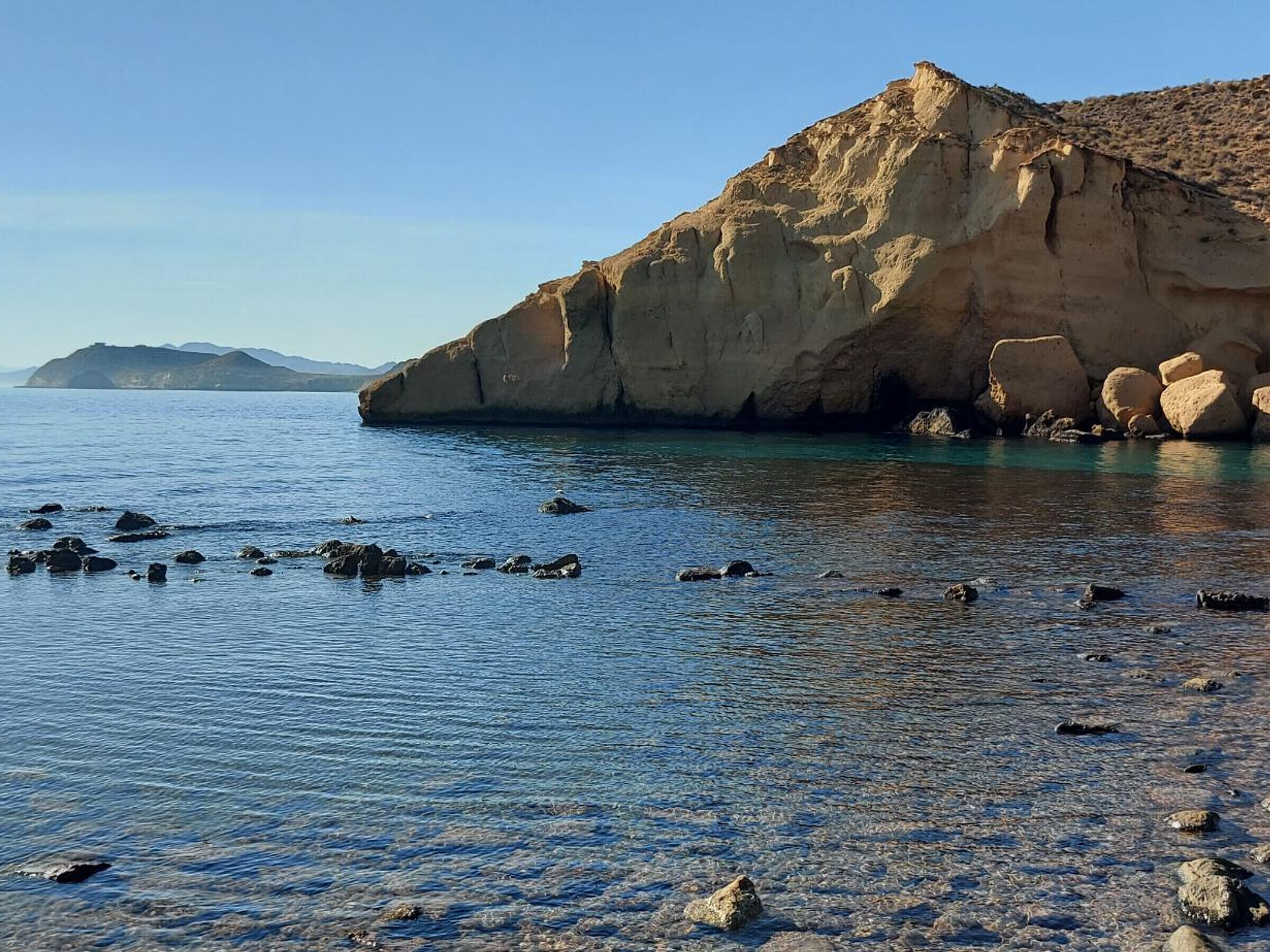 A coastal scene with a prominent rock formation and calm waters.