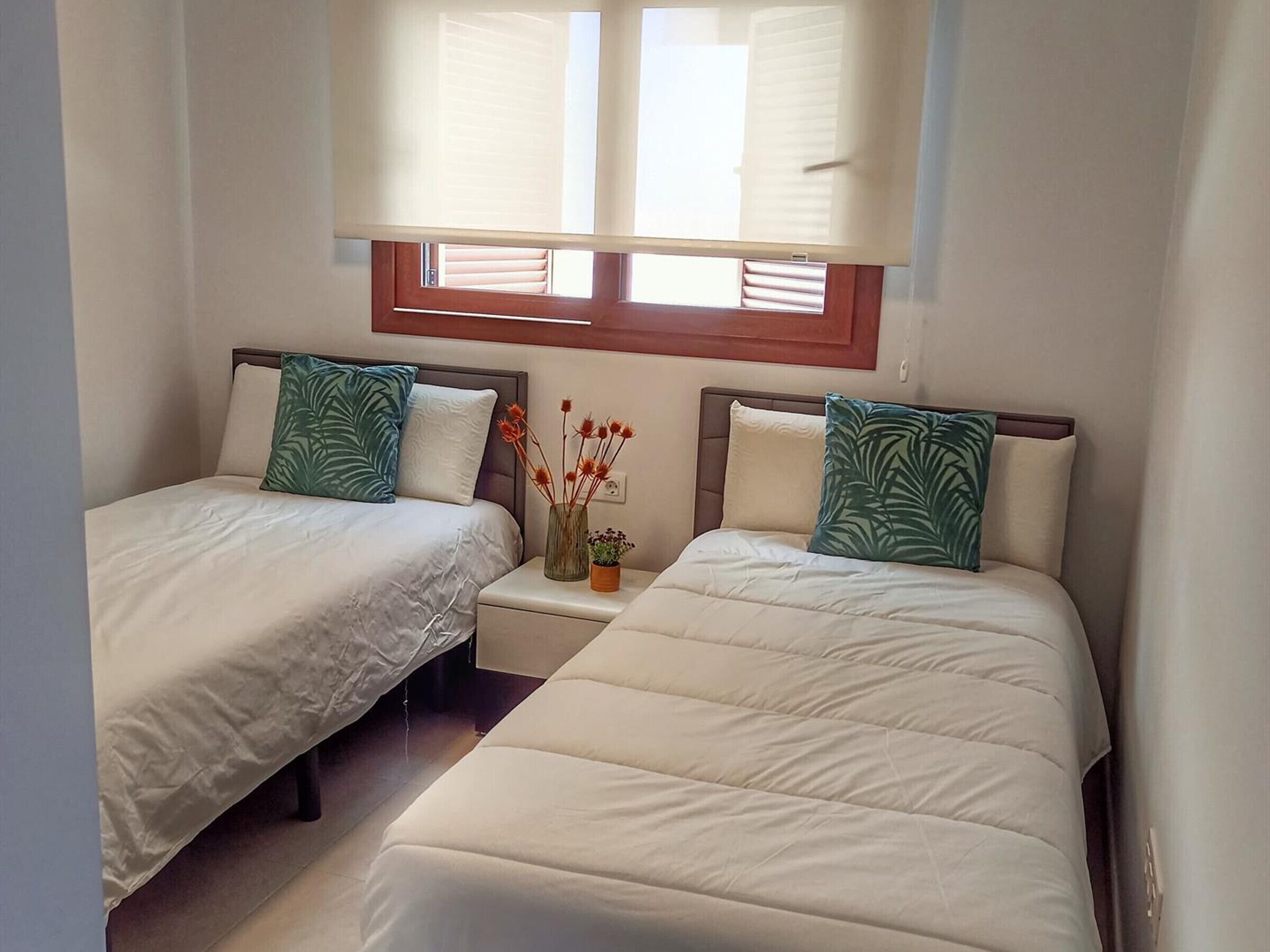 Een kamer met twee bedden, elk met een kussen en een nachtkastje met een vaas.