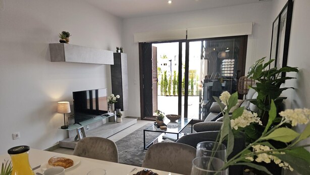 Un salon moderne doté d’un téléviseur à écran plat, d’une table à manger dressée pour le petit-déjeuner et d’une grande fenêtre donnant sur un jardin.