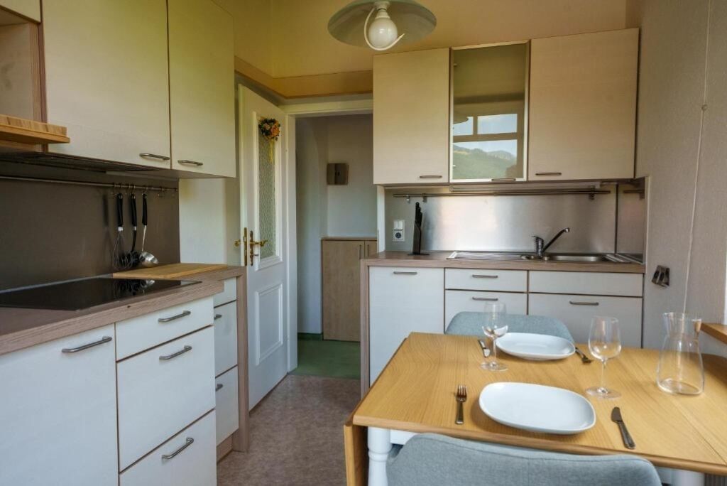 Eine kleine Küche mit weißen Schränken, einer Holzausziehtafel und einer Essecke mit Tisch für zwei Personen.