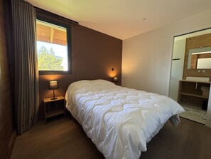 Un dormitorio con una cama grande, una mesita de noche con lámpara, una ventana con cortinas y un baño con espejo y lavabo.