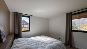 Ein Schlafzimmer mit einem großen Bett, zwei Fenstern und Blick auf ein Haus und Berge.