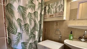 Une petite salle de bain équipée d’un lave-linge, d’un lavabo et d’un espace douche.