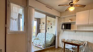 Un espace de vie compact comprenant un coin repas, un lit avec une literie à motifs, un ventilateur de plafond et une porte-fenêtre coulissante donnant sur un espace extérieur.