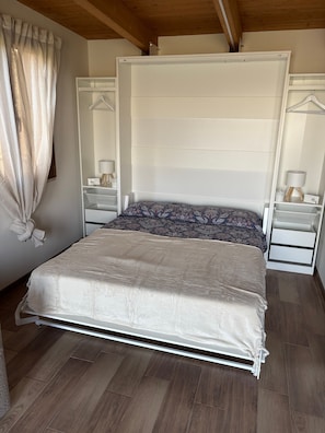 A bedroom with a bed, bedside tables, a hanging lamp, and a window with curtains.