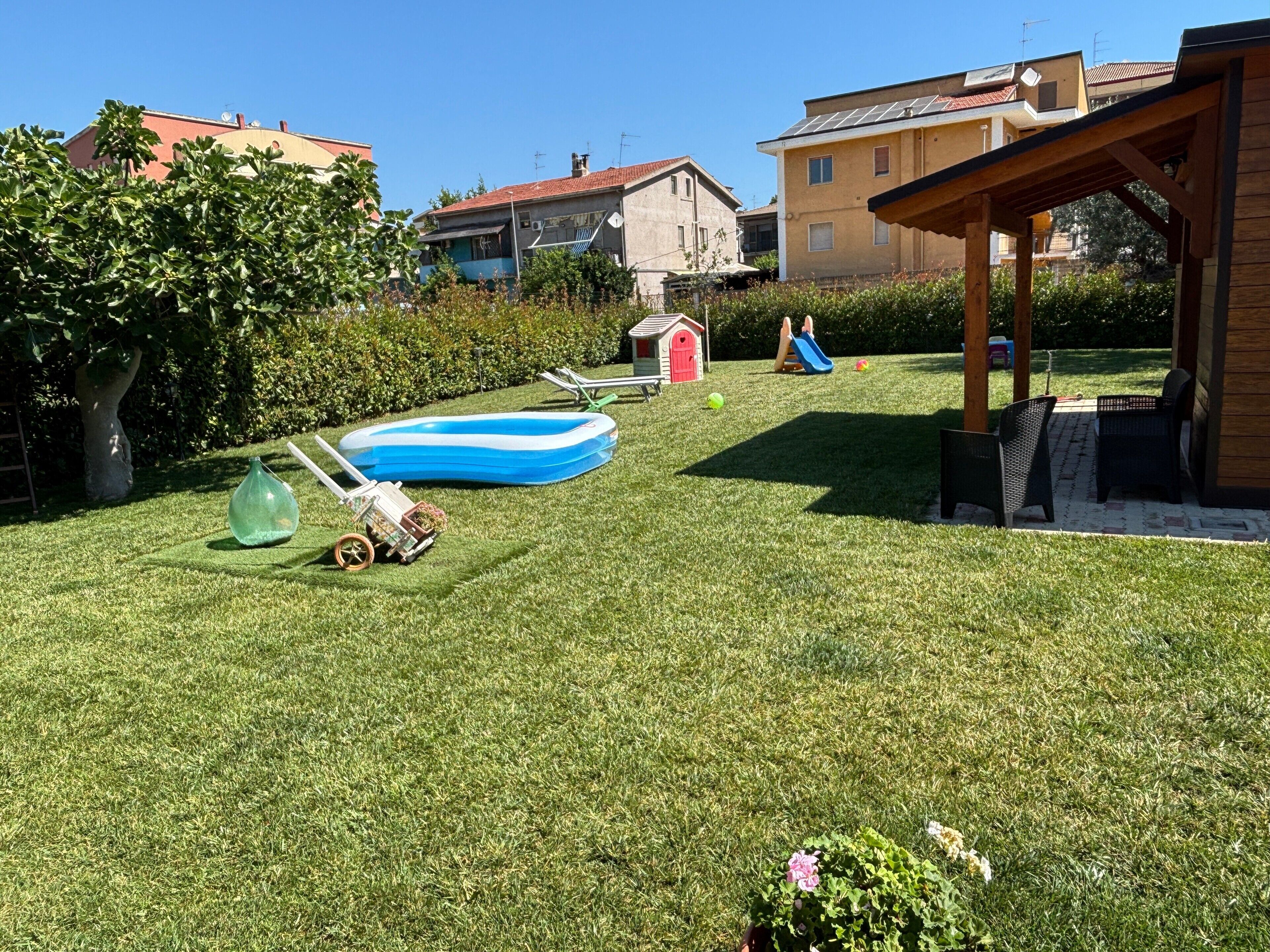 Ein gepflegter Rasen mit einem kleinen aufblasbaren Pool, einem Gartenhaus und einer Hollaube.