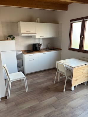 A compact kitchen with white cabinetry, a coffee maker, and a sink. There is a small wooden table and two white chairs.
