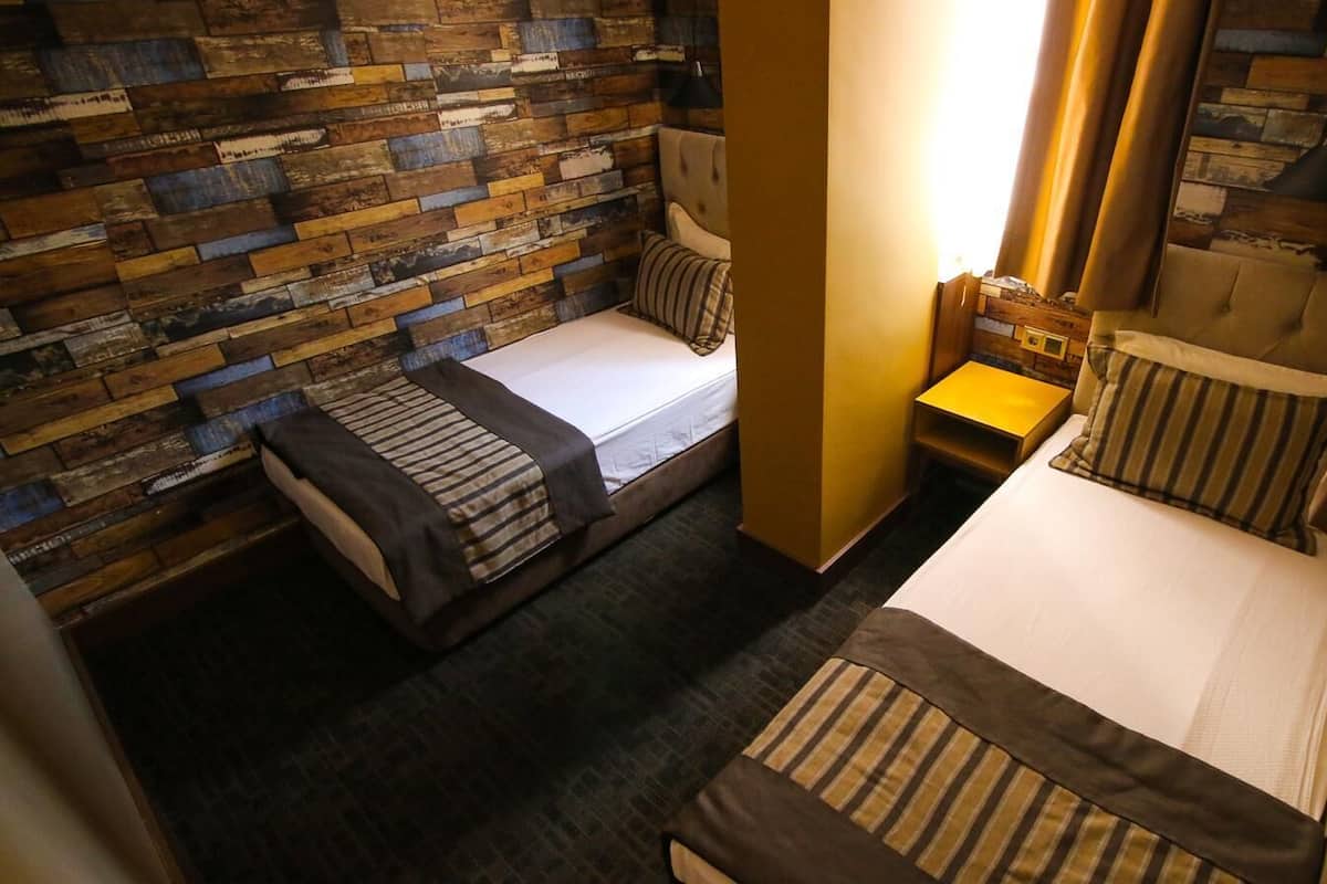 Una habitación pequeña y acogedora con dos camas individuales, una mesita de noche y una pared de madera decorativa.
