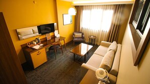 Habitación de hotel con sofá, mesa de centro, televisor, escritorio y una silla.
