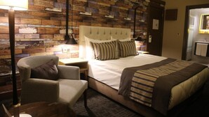 Habitación de hotel con una cama, una silla, una mesita de noche, una lámpara y un panel de pared con diseño de madera.