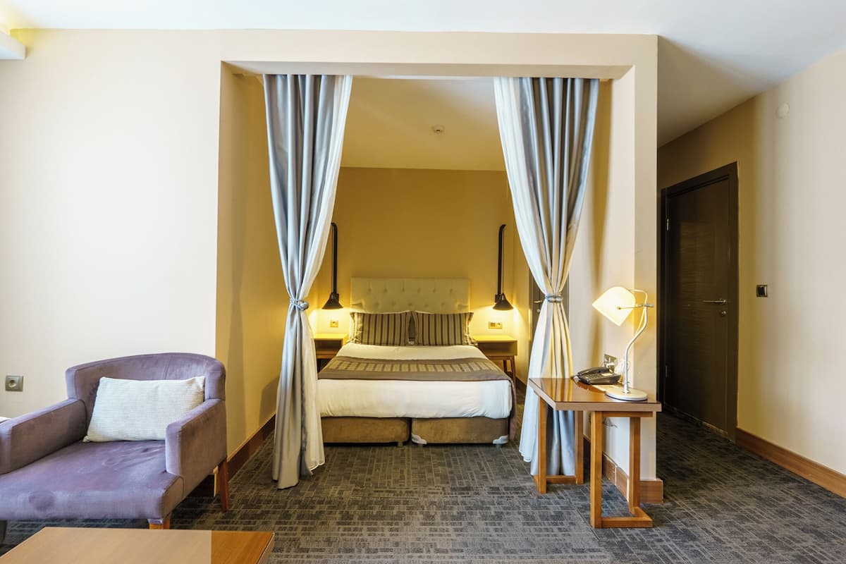 Una habitación de hotel con una cama, una silla, un escritorio con lámpara y cortinas.